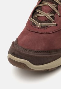 Brauner und kastanienbrauner Sport-Schuh mit Obermaterial aus Wildleder, Mesh-Akzenten, strukturiertem Sohlenprofil und hervorgehobenem dreieckigem Logo auf der Ferse.