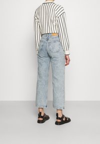 Avskuren vit tröja med svarta ränder som kombineras med ljusblå raka jeans och svarta sandaler, vilket visar en avslappnad passform och denimtextur.