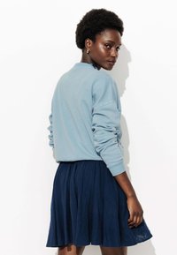 Sweatshirt bleu clair avec des poignets et un col côtelés, associé à une jupe plissée marine. Tissu texturé visible sur la jupe.