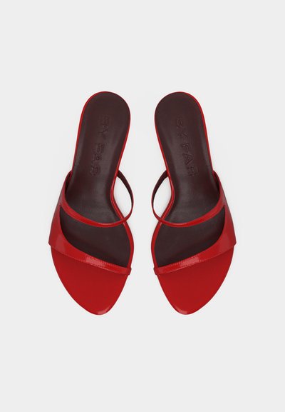 Pár červených otvorených šlapiek so tenkými remienkami a čiernymi vnútornými stielkami, zobrazených na bielom pozadí.