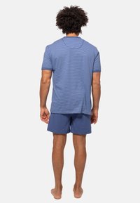 Manskavajset med en randig blå kortärmad skjorta och enfärgade blå shorts, tillverkade av mjukt tyg, med en avslappnad passform.