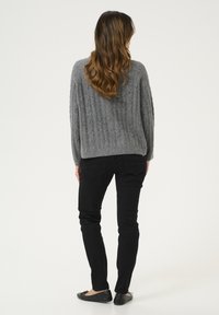 Pull en tricot gris avec texture côtelée, associé à un jeans noir ajusté et des chaussures plates. Vue de dos, mettant en avant une silhouette décontractée.