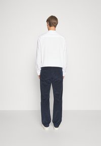 Camicia bianca a maniche lunghe con colletto standard, abbinata a pantaloni in corduroy blu navy. Texture liscia, design a gamba dritta, stile casual.