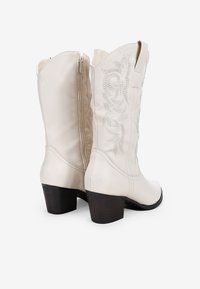 Botas de vaquero de cuero blanco con tacón bloque de altura media, decoradas con bordados de plata en el lado exterior y cierre con cremallera en la parte posterior.