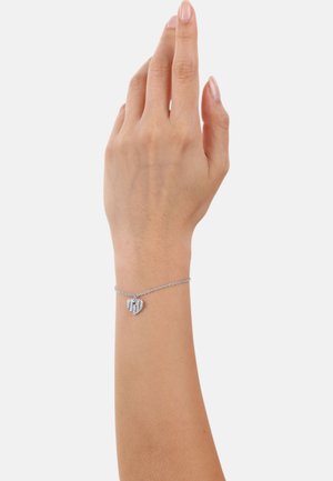 Bracciale in argento con un ciondolo a forma di cuore con dettagli a righe. La mano è leggermente sollevata, mettendo in mostra il design della gioielleria.
