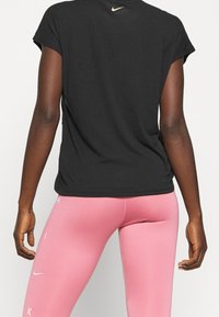 Camiseta negra de manga corta con cuello redondo y sutil logo dorado de Nike en la parte posterior, combinada con leggings rosas ajustados.