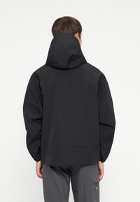 Black waterproof jacket with a hood, featuring elastic cuffs and a relaxed fit. Smooth texture, minimalistic design, no visible logos.