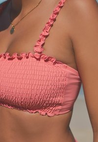 Top bikini rosa con arricciatura e spalline volant, realizzato in materiale testurizzato. Finitura liscia con dettagli arricciati lungo i bordi.