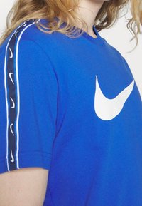 Sininen puuvillapaita, jossa on suuri valkoinen Nike-logo rinnassa. Hihoissa on musta-valkoraidat ja pienet logot.