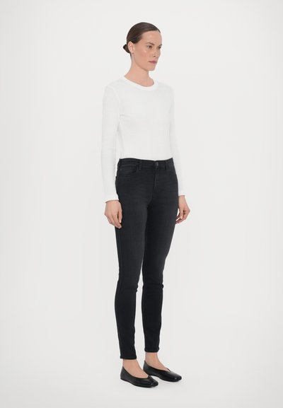 Svarta smala jeans med hög midja, ihopparat med en åtsittande vit långärmad topp. Platta svarta skor fulländar outfiten.