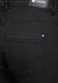 Svarta denimjeans med en bakficka, subtila sömdetaljer och en etikett på midjebandet som säger "Street One."