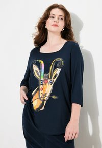 Tummansininen pitkähiha-paita, jossa on värikäs vuohigrafiikka, jossa on sarvet, sydän ja vehnäkoristelua. Pehmeä, rento istuvuus.