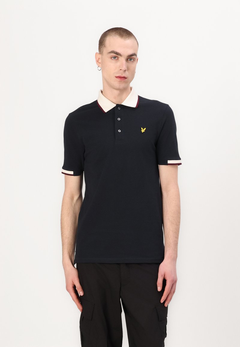 Marinblå polo skjorta med beige krage och vinröd trim, med tre-knappars knäppning och gult broderat logotyp på vänster bröst.