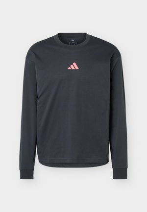 Czarna koszulka z długim rękawem i okrągłym dekoltem z małym różowym logo Adidas na środku klatki piersiowej, pokazana na jednolitym tle.