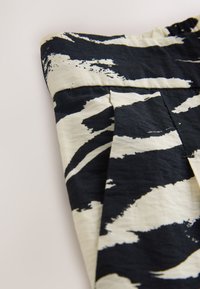 Tissu à motif abstrait noir et blanc avec une couture visible et une ceinture partiellement froncée.