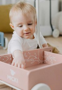 Trækdyr lavet af træ med en pink krop og hvide illustrationer af skyer og dyr indeni. Har et håndtag og rullende hjul.