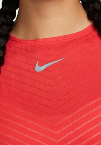 Punainen Nike-urheilupaita, jossa on teksturoitu, kevyt kangas ja vinoneliökuvio. Vaaleansininen logo keskitettynä lähellä kaula-aukkoa.