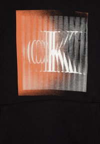 Felpa nera con cappuccio, caratterizzata da un design grafico con tonalità di arancione e grigio sfumate, che mostra del testo bianco frammentato in uno stile audace e distorto.