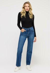 Maglione nero a maniche lunghe con collo a lupetto abbinato a jeans blu a vita alta e sneakers bianche, con tasche e design dritto.