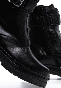 Bottines en cuir noir avec semelles épaisses en caoutchouc, fermetures éclair latérales et sangles à boucle près du haut.