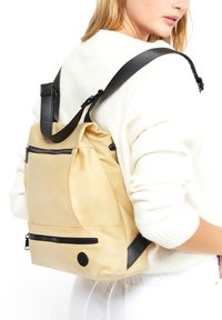 Zaino impermeabile giallo con accenti neri, singolo strap regolabile, tasche con cerniera e silhouette arrotondata. Texture liscia.