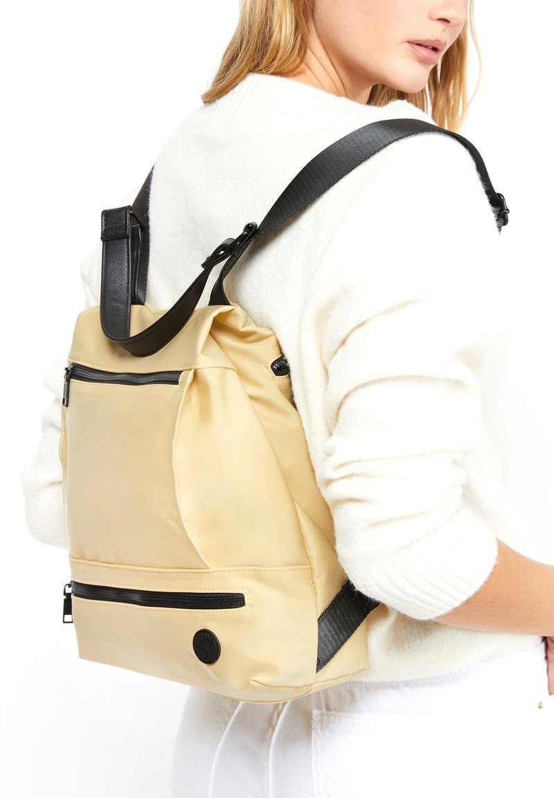 Zaino impermeabile giallo con accenti neri, singolo strap regolabile, tasche con cerniera e silhouette arrotondata. Texture liscia.