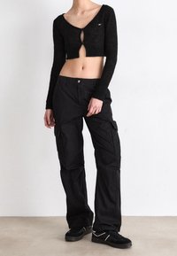 Suéter negro corto con cierre de botón; combinado con pantalones cargo negros holgados que tienen bolsillos laterales. Zapatillas negras completan el atuendo.