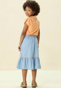 Haut court à manches courtes orange clair et jupe en denim bleu à volants avec une taille élastique et des coutures orange. Sandales plates.