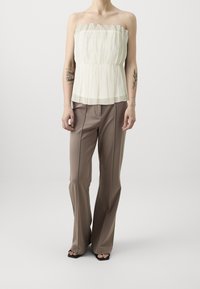 Top trasparente senza spalline con volant in sfumature e cintura elastica, abbinato a pantaloni beige a vita alta e gamba larga in tessuto liscio.