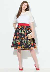 Ein Floral-Druckrock in Schwarz mit einem roten Taillenbund und Akzenten, kombiniert mit einem weißen Spitzentop. Die Accessoires umfassen eine kleine geflochtene Tasche.