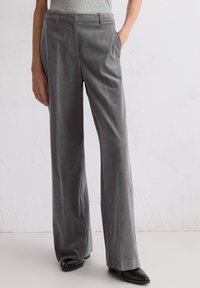 Szare szerokie spodnie z kordówki o gładkiej fakturze, z przednimi kieszeniami i dopasowanym krojem. Noszone z czarnymi butami na obcasie.