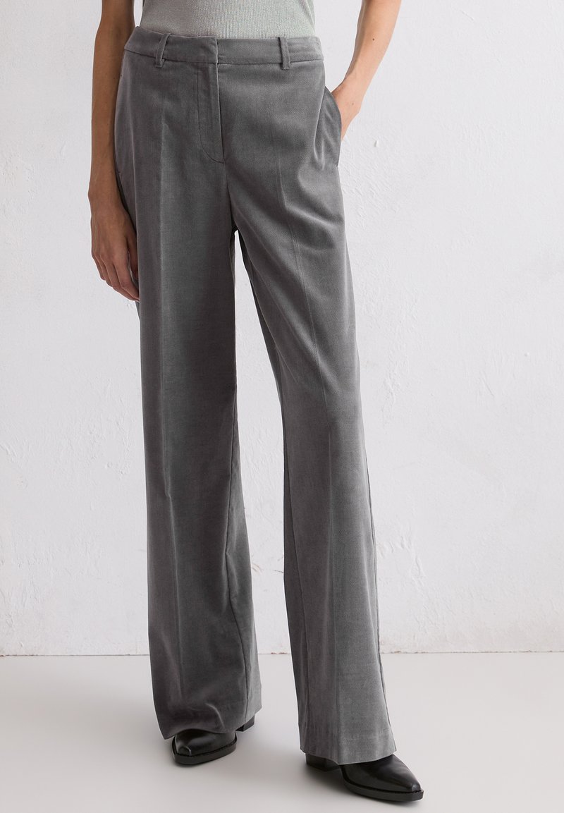 Szare szerokie spodnie z kordówki o gładkiej fakturze, z przednimi kieszeniami i dopasowanym krojem. Noszone z czarnymi butami na obcasie.