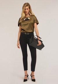 Blusa di raso oliva a maniche corte, pantaloni neri aderenti e una borsa nera. Scarpe nere con tacco e una collana statement con diverse forme.
