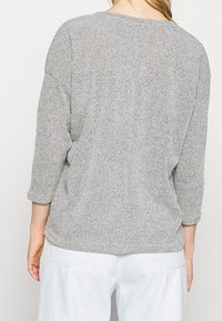Ljusgrå stickad tröja med en avslappnad passform, trekvartsärmar, texturerad tyg och en enkel rund halsringning.