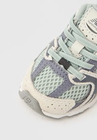 Αθλητικό παπούτσι σε ανοιχτό τιρκουάζ με υφή από δίχτυ και σουέντ, που διαθέτει γκρι λεπτομέρειες, κορδόνια και ενισχυμένη μύτη.