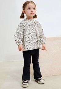 Floral patterned blouse with gathered neckline and long sleeves, paired with black flared trousers and black sneakers.