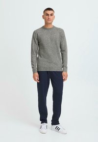 Suéter de punto gris con mangas largas y cuello redondo; combinado con pantalones jogger azul marino y zapatillas blancas con rayas negras.