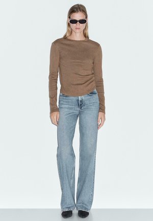 Brown long-sleeve top, light blue flared jeans, and black sunglasses. Smooth texture with fitted bodice and casual silhouette.