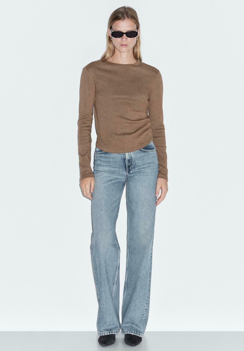 Brown long-sleeve top, light blue flared jeans, and black sunglasses. Smooth texture with fitted bodice and casual silhouette.