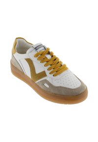 Sneaker bianca con una punta in suede marrone chiaro e una striscia gialla in evidenza, dotata di lacci gialli e suola in gomma. Progettata per il comfort.