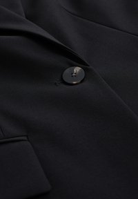 Schwarze Blazer mit glattem Stoff, einem runden Knopfverschluss und strukturiertem Revers. Schlichte und minimalistische Ästhetik.