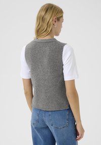 Grauer Strickwestenpullover aus Strickstoff, mit rundem Ausschnitt, ärmellosem Design, kombiniert mit einem weißen T-Shirt und blauen Jeans.