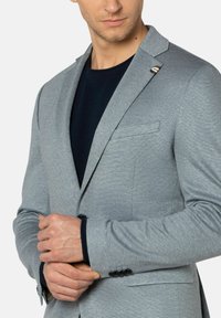Grijze blazer met een subtiele textuur, slim fit, met notch revers en een enkele knoopsluiting. Beschikt over contrasterende donkere manchetten en een zakdetail.