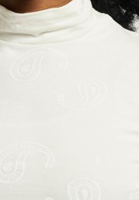 Chandail à col montant blanc avec un motif paisley subtil, texture lisse et design ajusté.