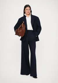 Marineblauwe op maat gemaakte oversized blazer en wijde broek, gecombineerd met een witte blouse. Bruine leren tas met gouden hardware, gladde textuur.