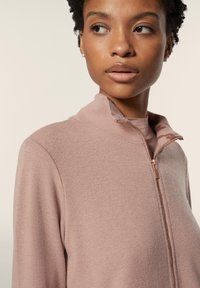 Felpa rosa chiaro con zip e collo alto, dalla texture morbida e con zip in rosetto. Design aderente con sottile dettaglio di texturizzazione.