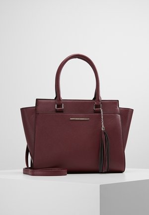 Dunkelrote Ledertasche mit doppelten Henkeln, einem Front-Quastenanhänger und einem abnehmbaren Schulterriemen auf einer weißen Oberfläche.