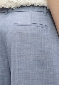 Κοντινό πλάνο ενός προσώπου που φοράει ανοιχτό μπλε παντελόνι με ραμμένη πίσω τσέπη και λευκό υφασμάτινο τοπ.