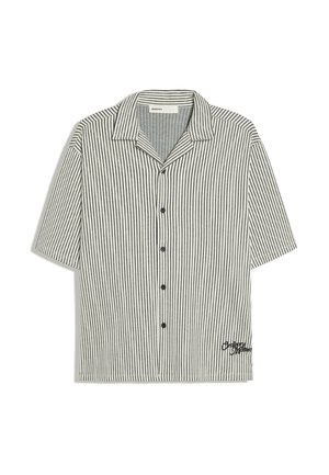 Chemise à manches courtes boutonnée avec des rayures verticales noires et un petit détail brodé près de l'ourlet sur fond blanc.