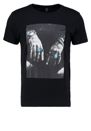 Sort T-shirt med grafisk tryk af hænder prydet med turkise ringe og armbånd, med indviklede tatoveringsdesigns synlige.